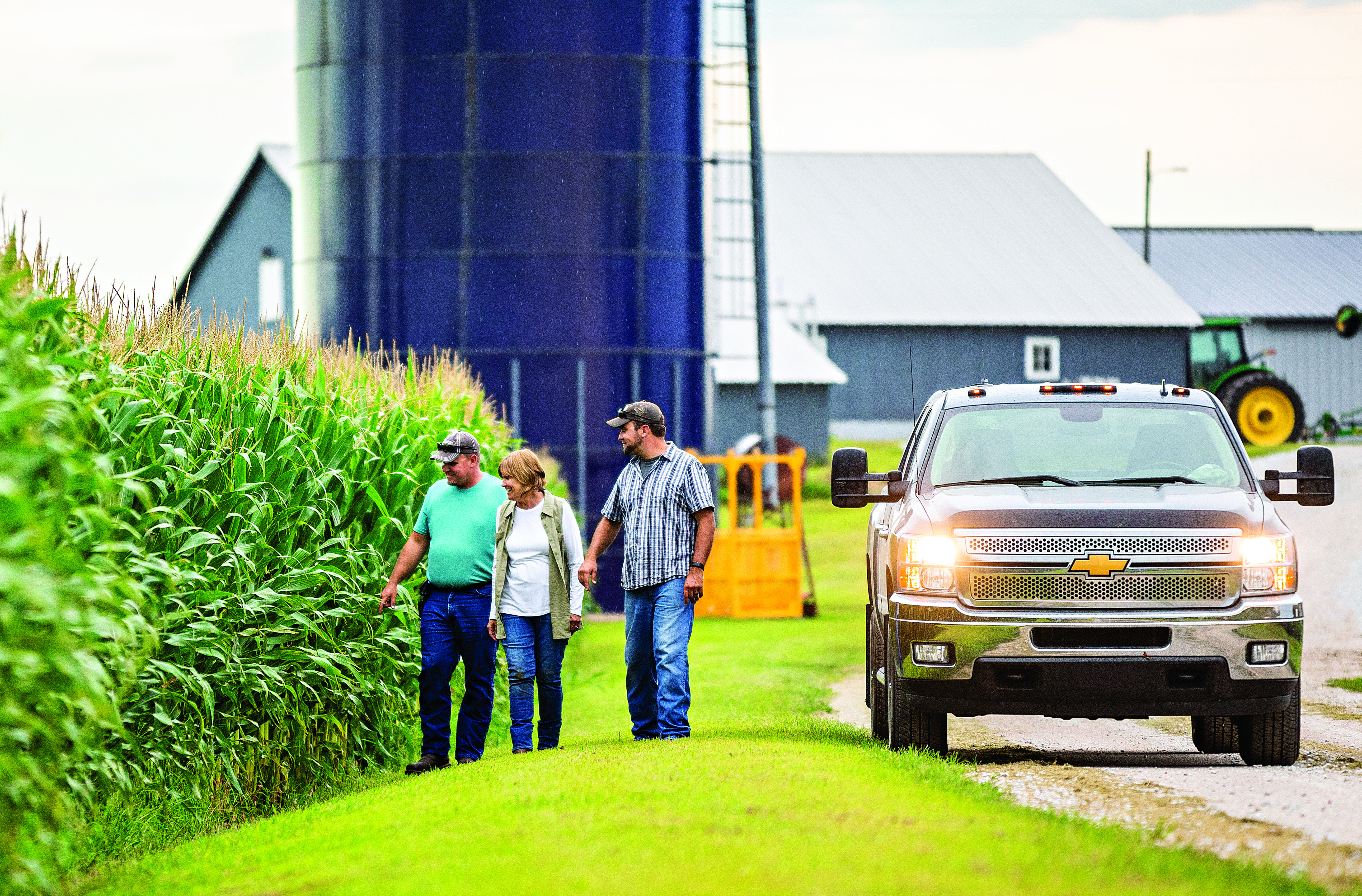 3 people walking by a pickup looking at corn